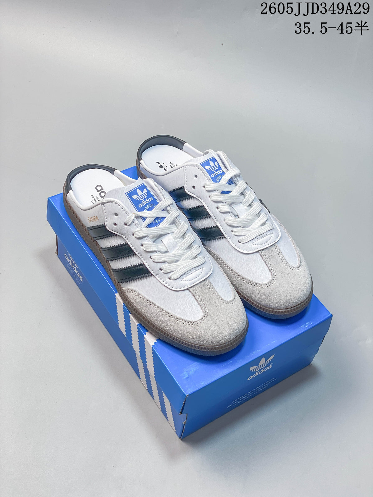 Pair of white Samba OG-style mule sneakers with dark stripes and gum-colored soles, shown on a blue shoebox.
