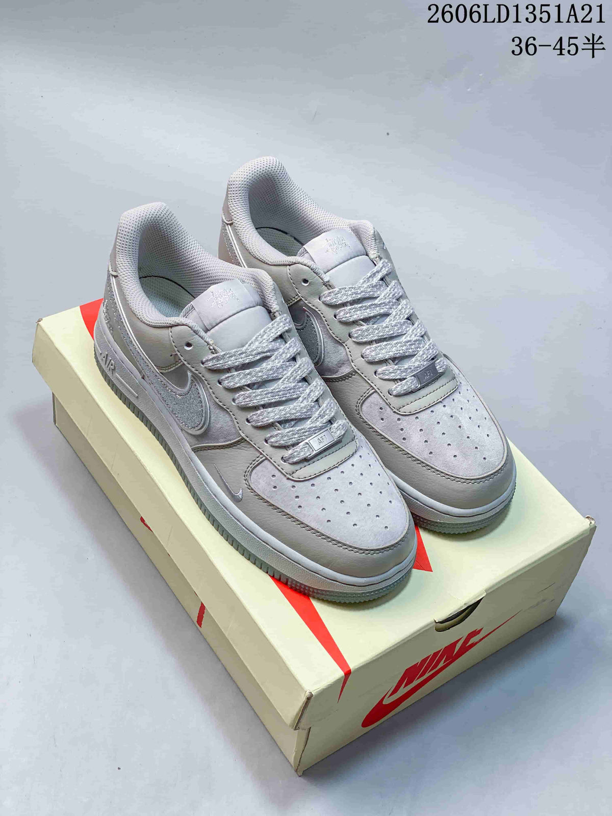 Pair of light gray Nike Air Force 1 low-top sneakers with silver-toned details on a shoebox