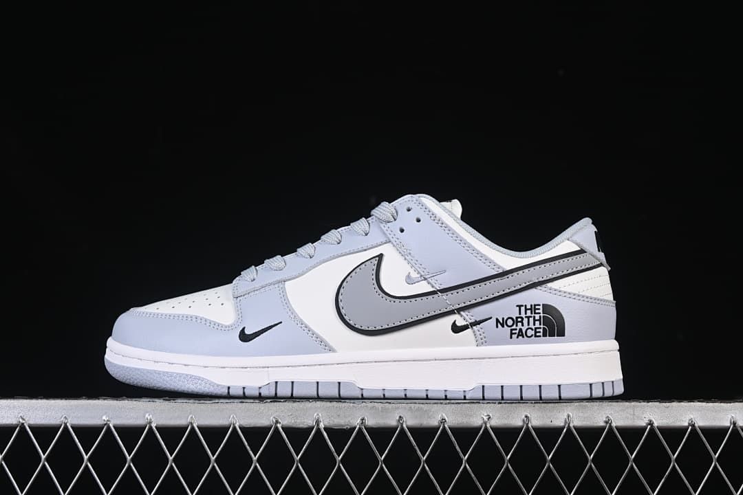 Side view of a white and light gray low-top sneaker with North Face graphics on the heel