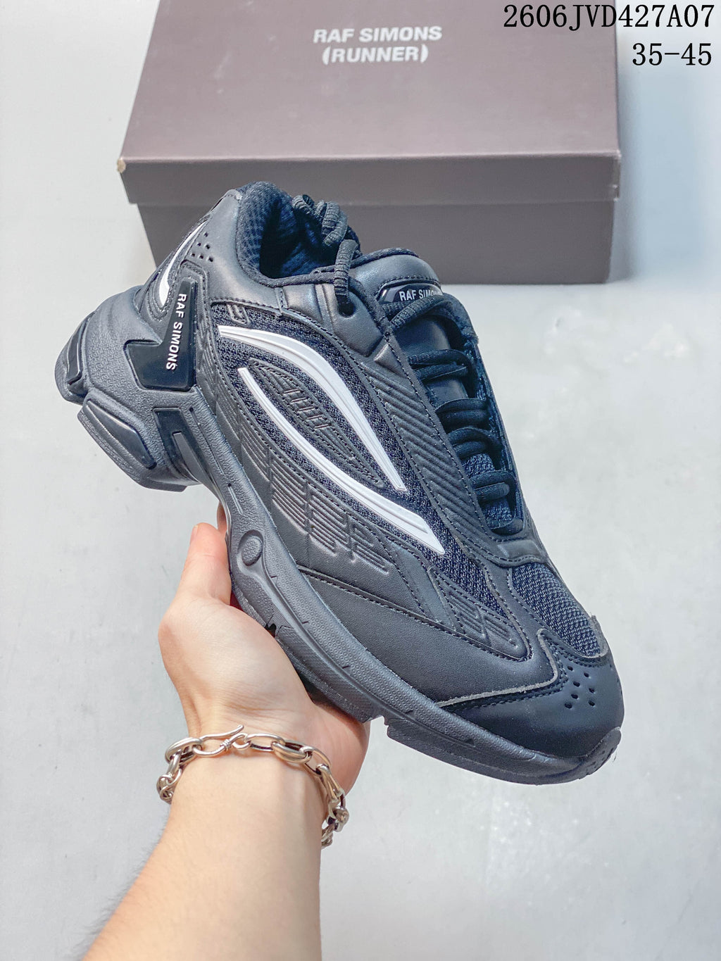 Angled side view of a charcoal Raf Simons sneaker with layered panels and light accents