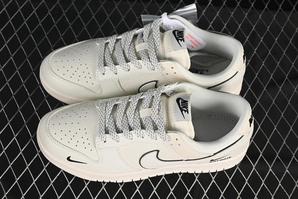 Top view of off-white Nike SB Dunk Low sneakers with patterned laces, perforated toe panels, and black Swoosh details.