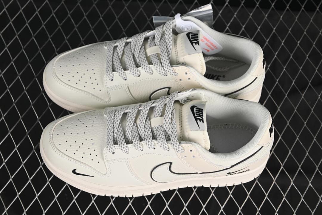 Top view of off-white Nike SB Dunk Low sneakers with patterned laces, perforated toe panels, and black Swoosh details.