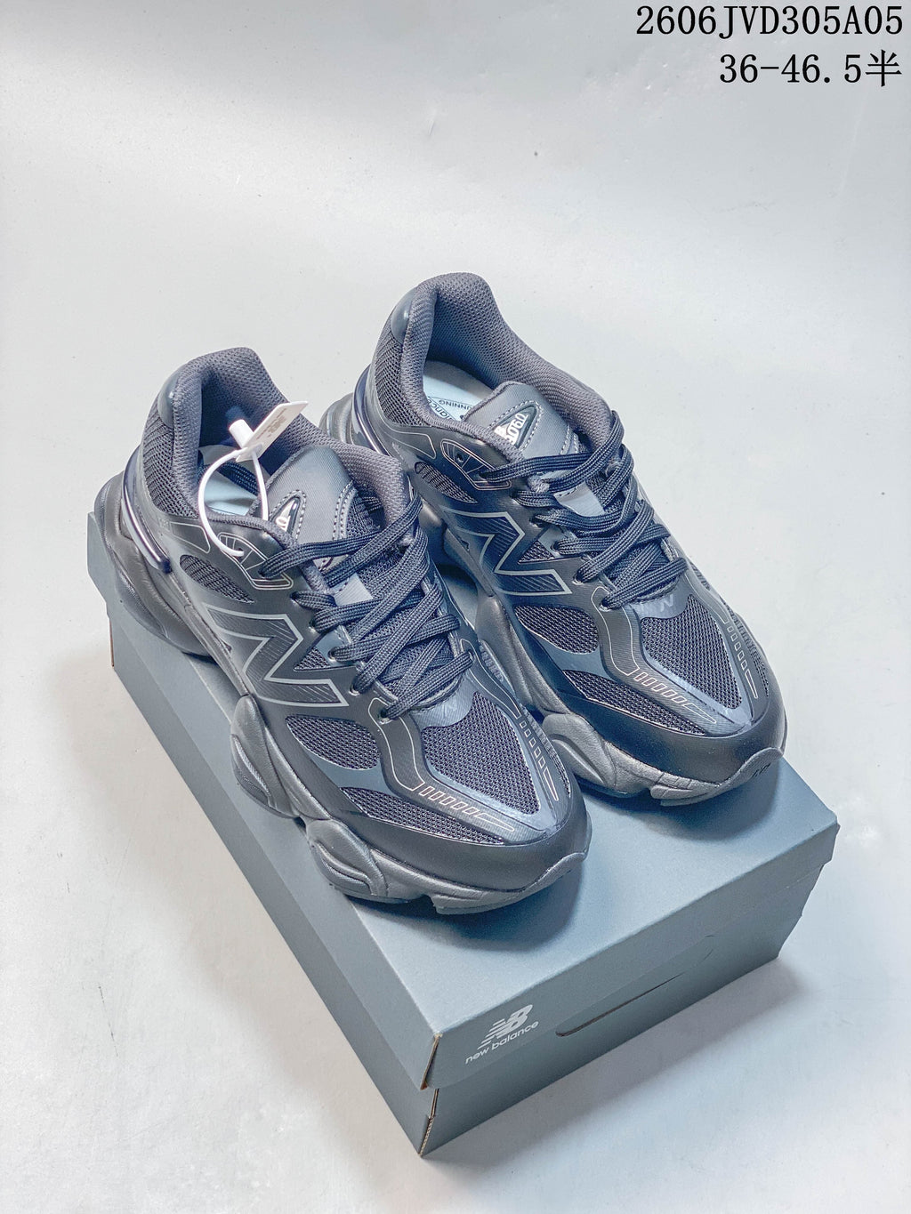 Pair of dark gray and navy New Balance 9060-style sneakers displayed on a shoebox.