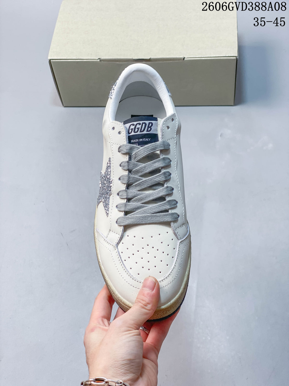 Front view of white sneaker with gray laces, perforated toe, and silver glitter star