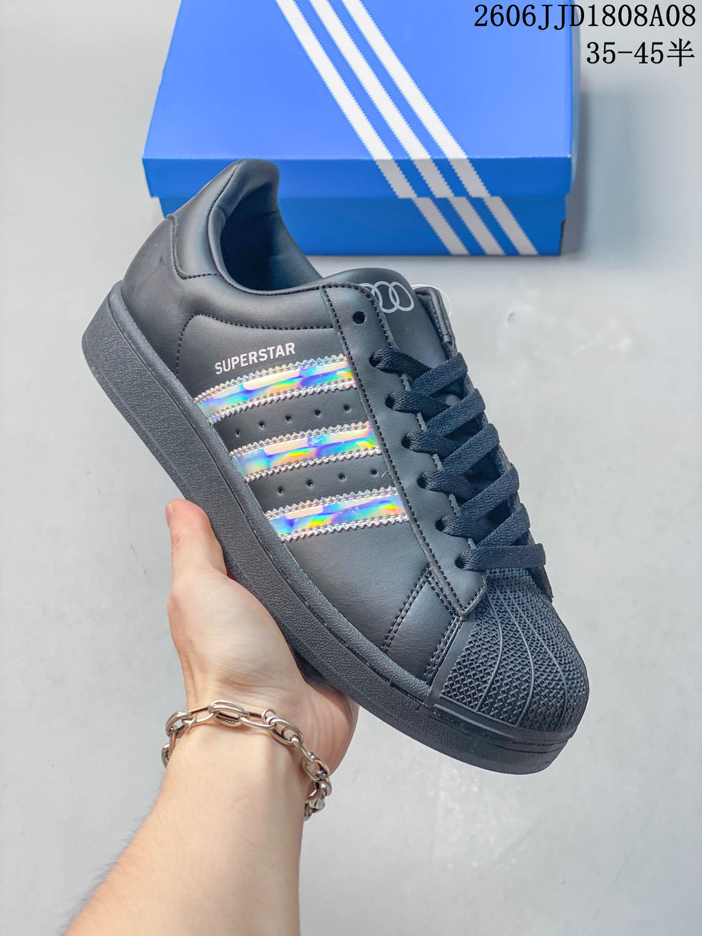 Angled side view of a charcoal Adidas Superstar sneaker with iridescent stripes.