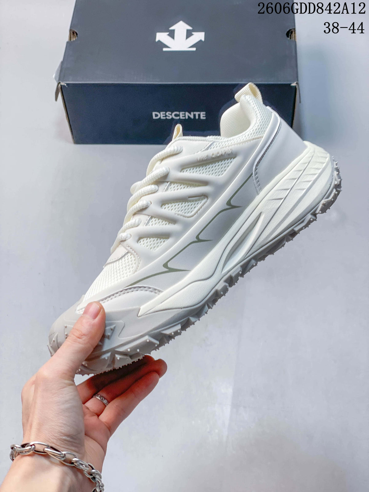 Side view of a white DESCENTE sneaker with mesh-style panels and a sculpted sole; the image displays size range 38–44.