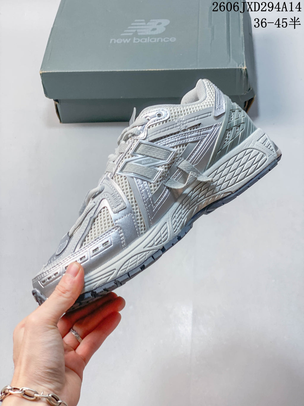 Side profile showing the layered upper and sole of a silver-grey New Balance 1906 sneaker.