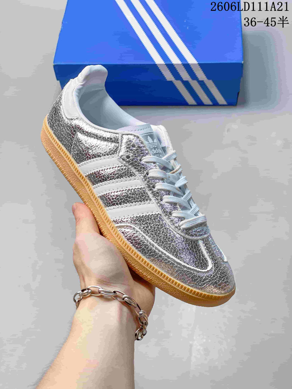 Close side view of a silver-toned sneaker with white stripes and a gum-colored outsole