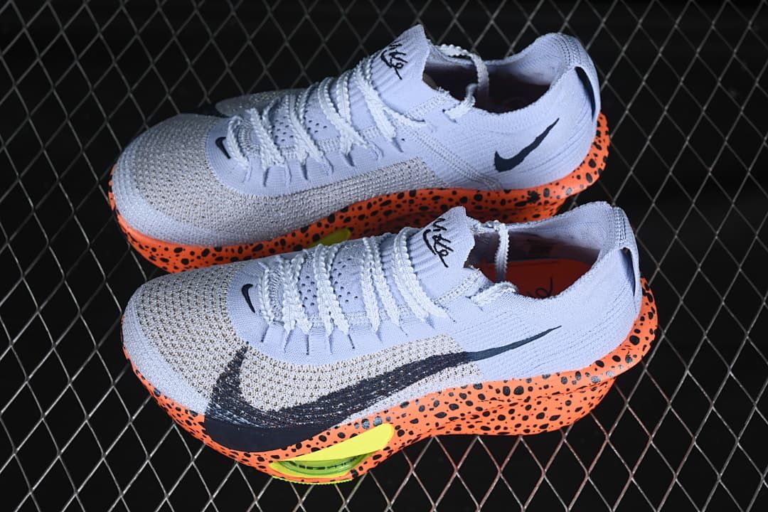 Pair of pale lavender racing shoes with orange-and-black speckled soles.