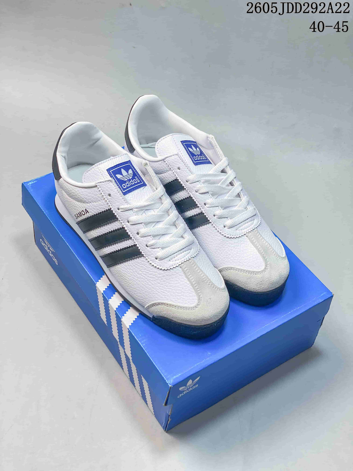 Pair of white Adidas Samoa low-top sneakers with dark stripes displayed on a blue shoe box