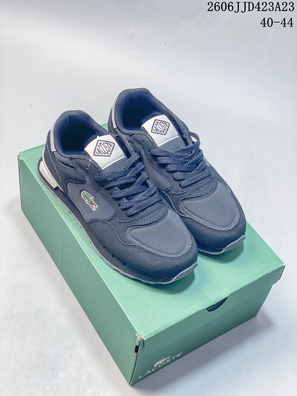 Pair of navy Lacoste-style low-top lace-up sneakers displayed on a green shoe box