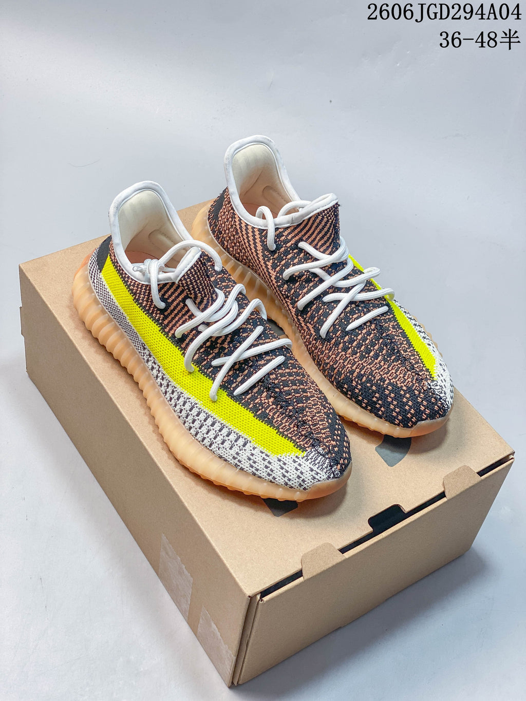 Pair of patterned Adidas Yeezy Boost 350 V2 sneakers with white laces, bright yellow side stripes, amber-toned soles, and a box