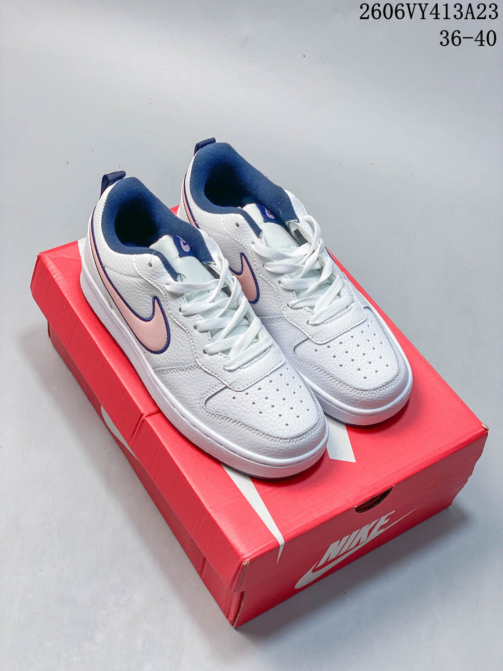Pair of white NikeCourt Borough 2 Low sneakers with pink Swooshes and navy details on a red box