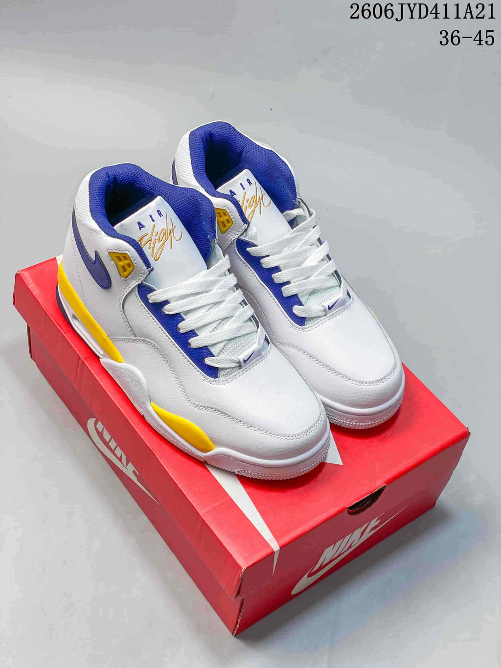 Pair of white Nike Flight Legacy mid-top sneakers with blue and yellow accents on a red shoebox