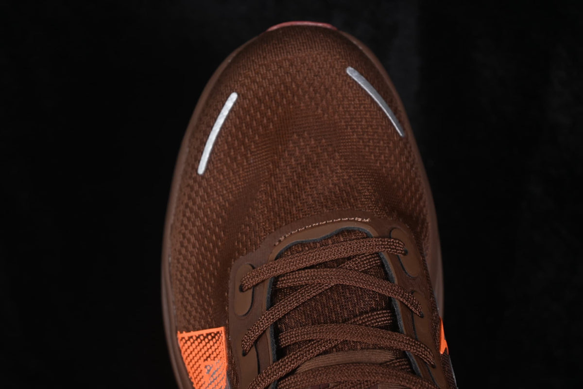 Top-down close-up of the brown textile toe box, brown laces, orange side detail, and reflective toe strips.