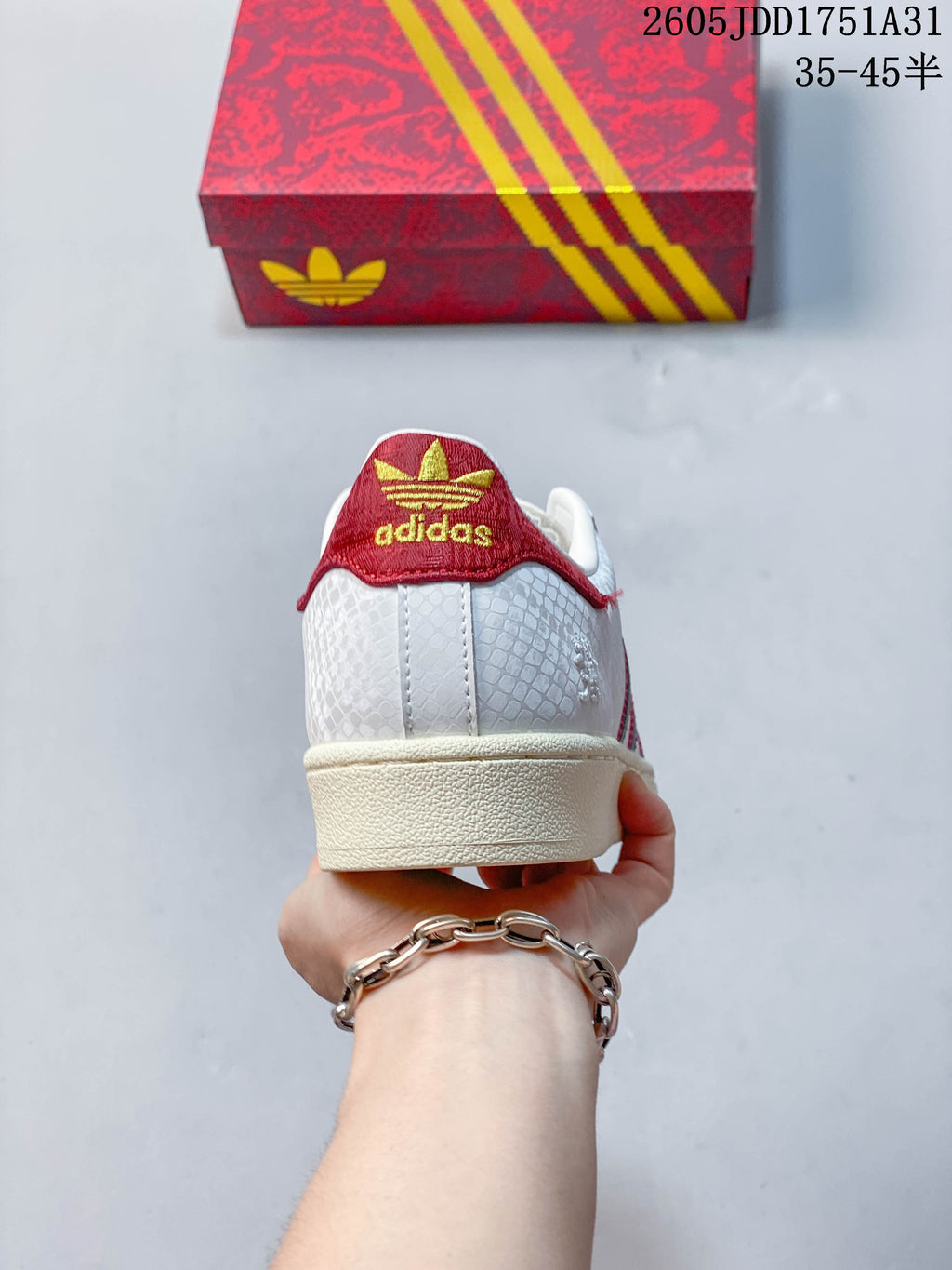 Rear view of a white Adidas Superstar sneaker with a red heel detail