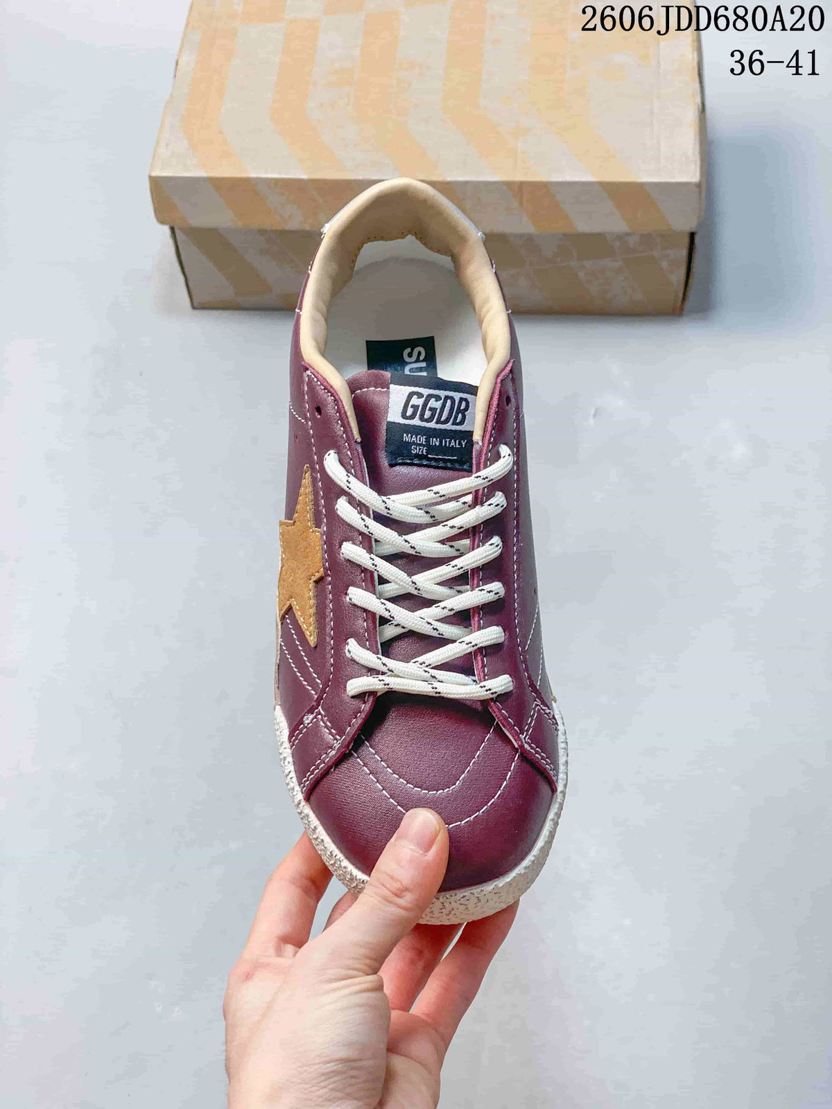 Front view of a burgundy lace-up sneaker with a tan side star and off-white toe bumper