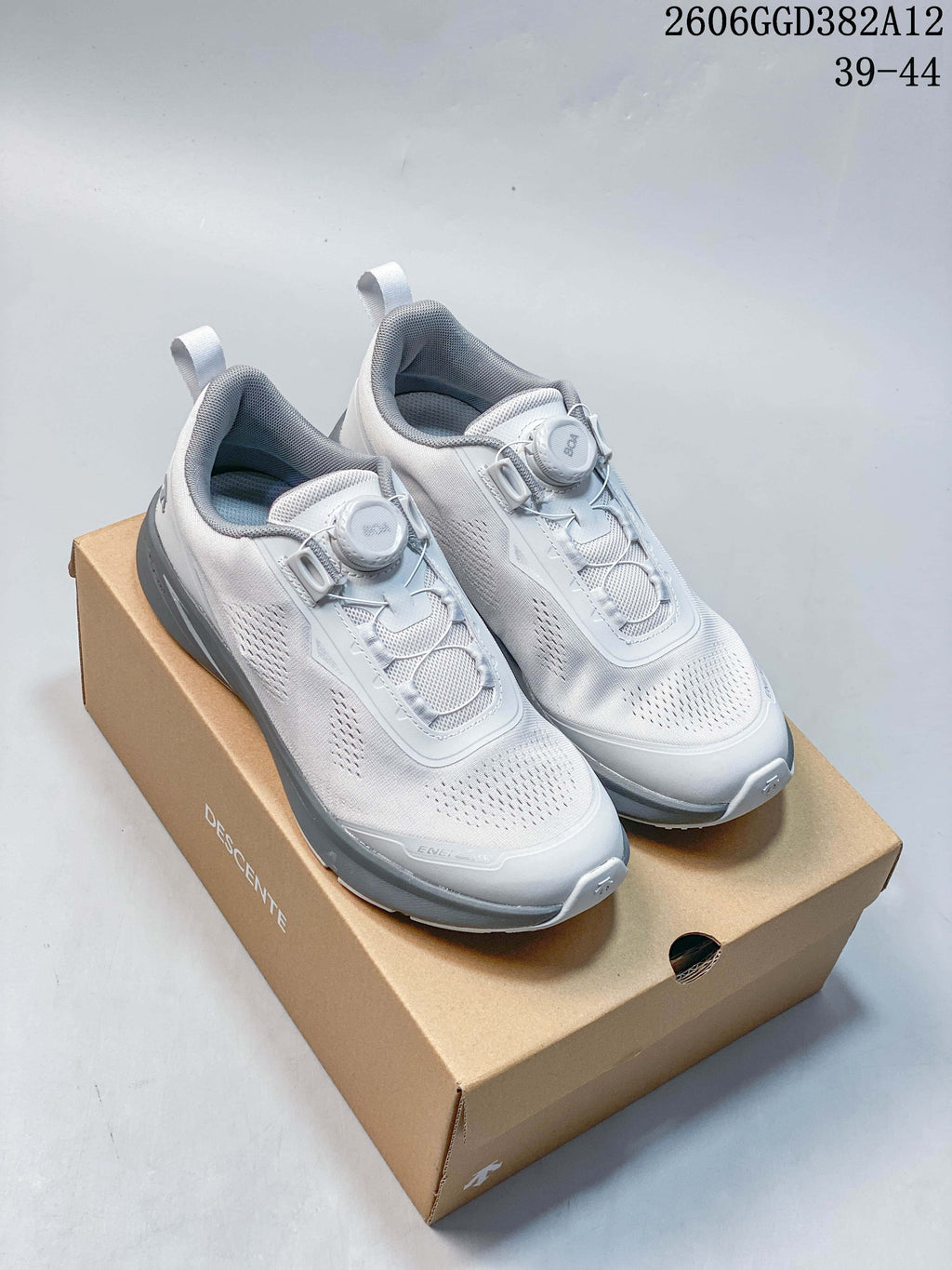 White and grey DESCENTE running shoes with dial closures displayed on a branded box.