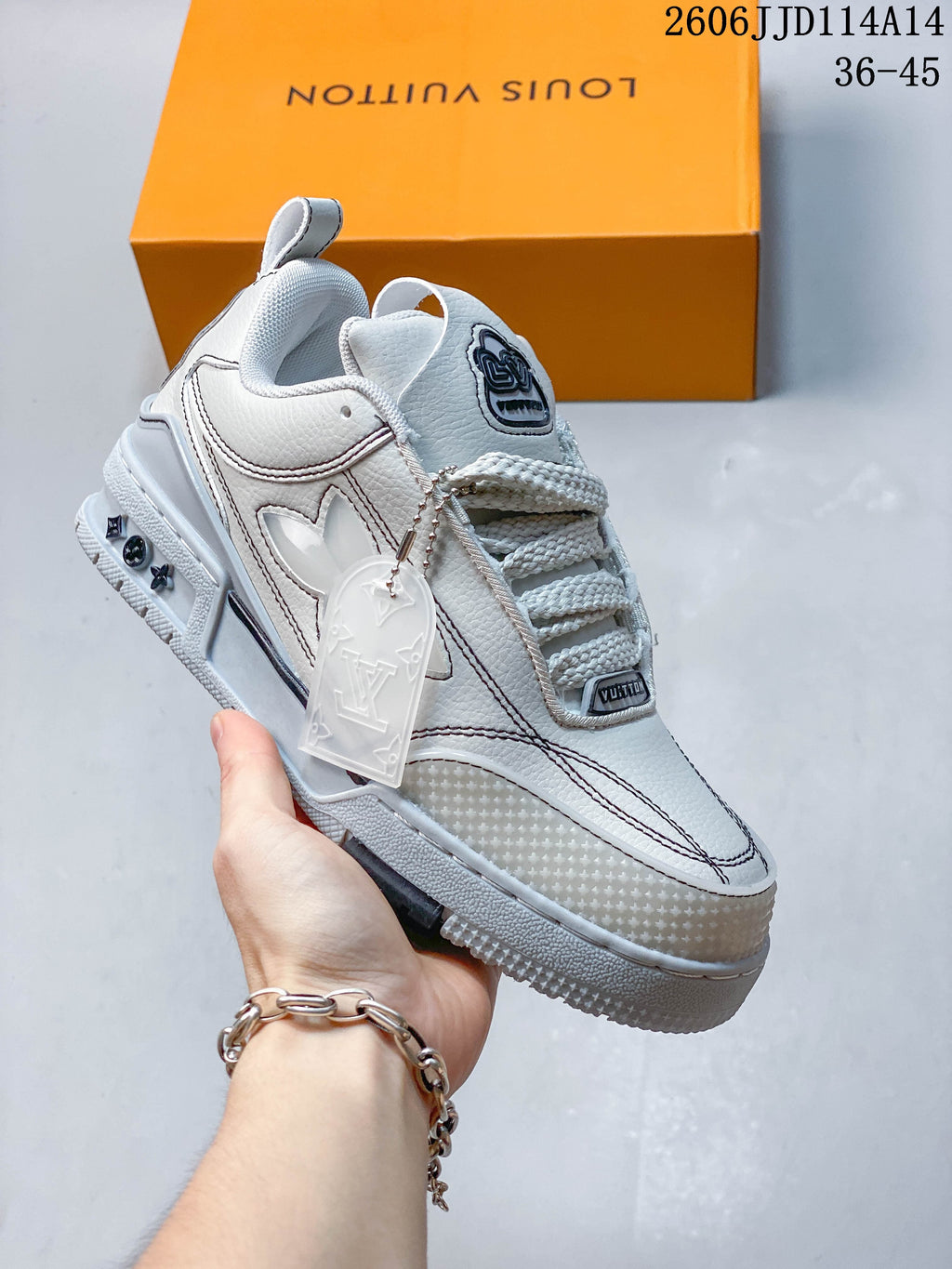 Angled side view of a white and gray Trainer sneaker with a hanging logo tag.