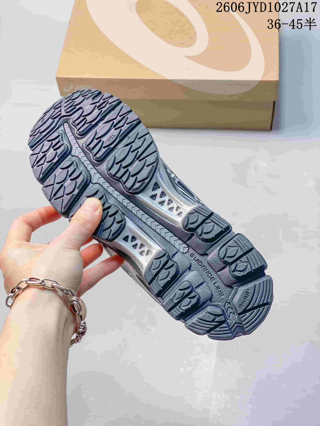 Treaded outsole of a dark gray sneaker, with an ASICS shoebox in the background