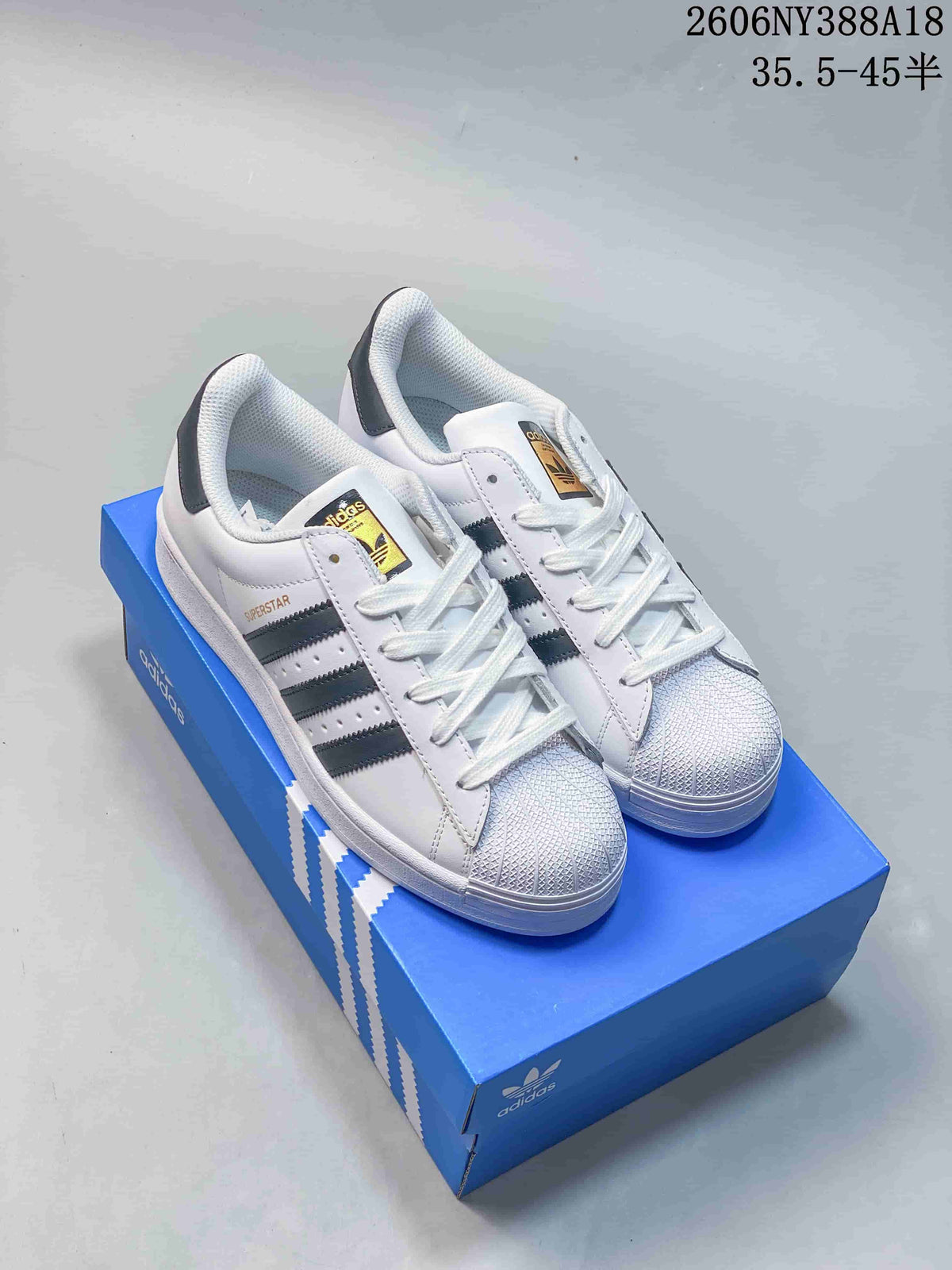 Pair of white Adidas Superstar low-top sneakers with dark stripes and shell-style toe caps, shown on a blue box.