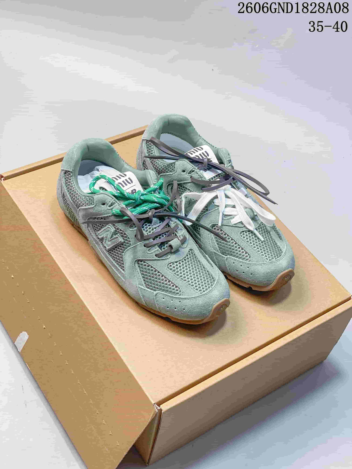 Pair of sage-green Miu Miu and New Balance sneakers with mesh panels, layered overlays and extra lace options, displayed on a box.