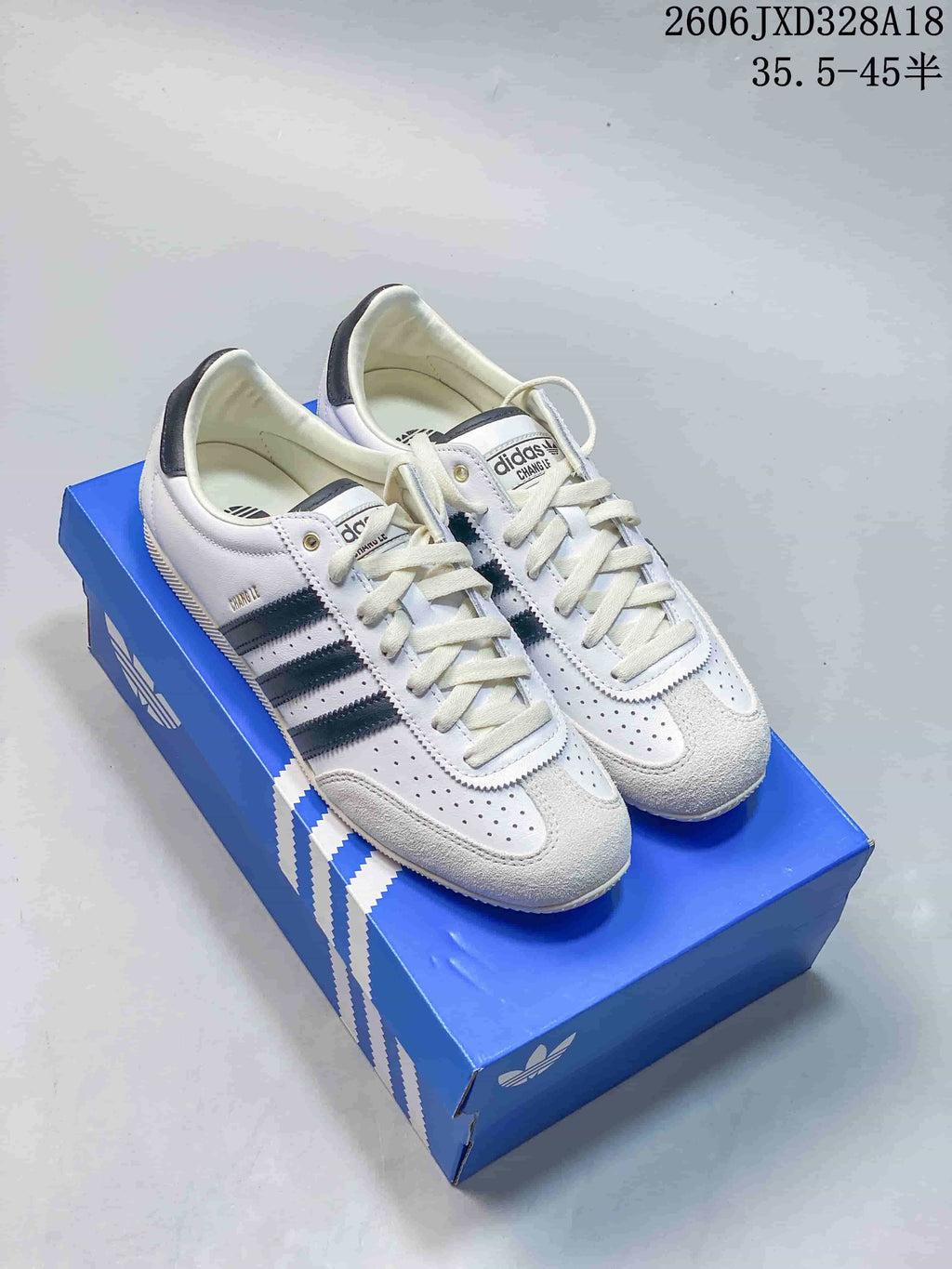 Pair of white adidas Originals Japan sneakers with dark stripes, shown on a blue shoebox