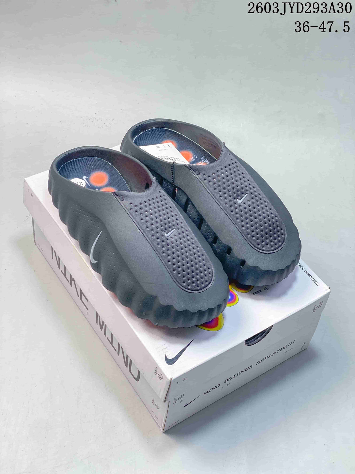 Pair of dark gray Nike Mind slides on a Nike Mind box
