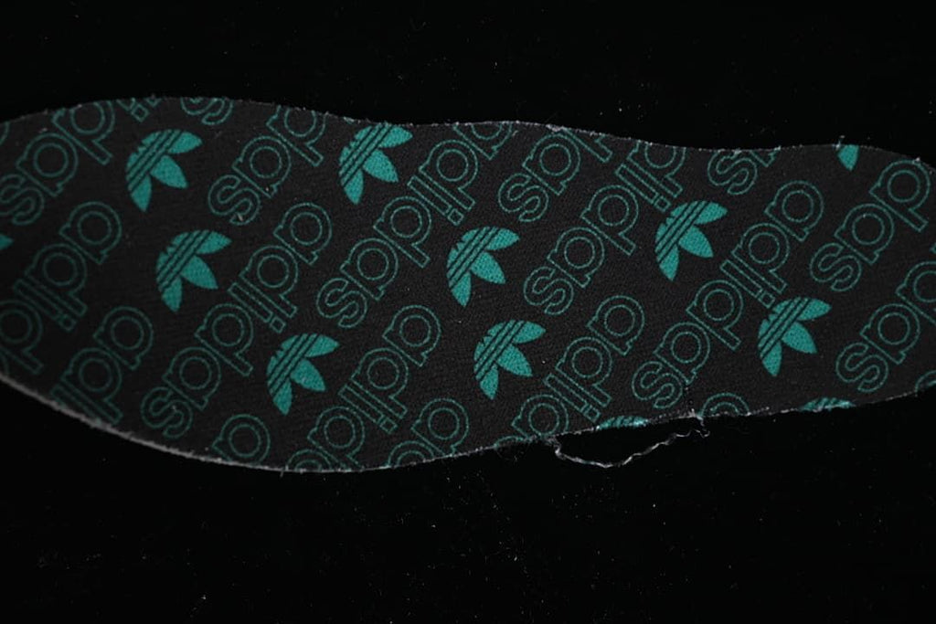 Close-up of a dark insole printed with teal adidas-style logos