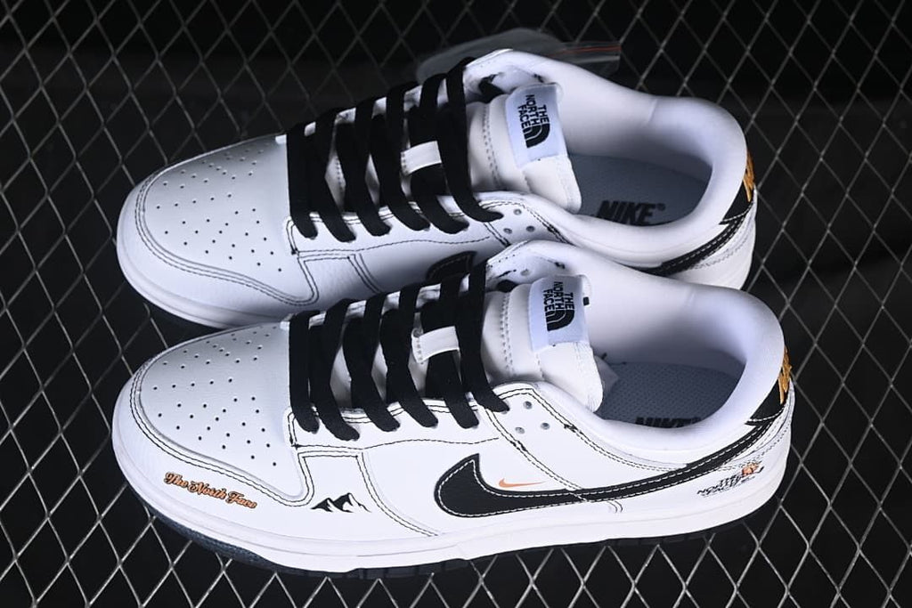 Pair of white and black low-top sneakers shown from above, with perforated toe boxes, black laces, and graphic details.