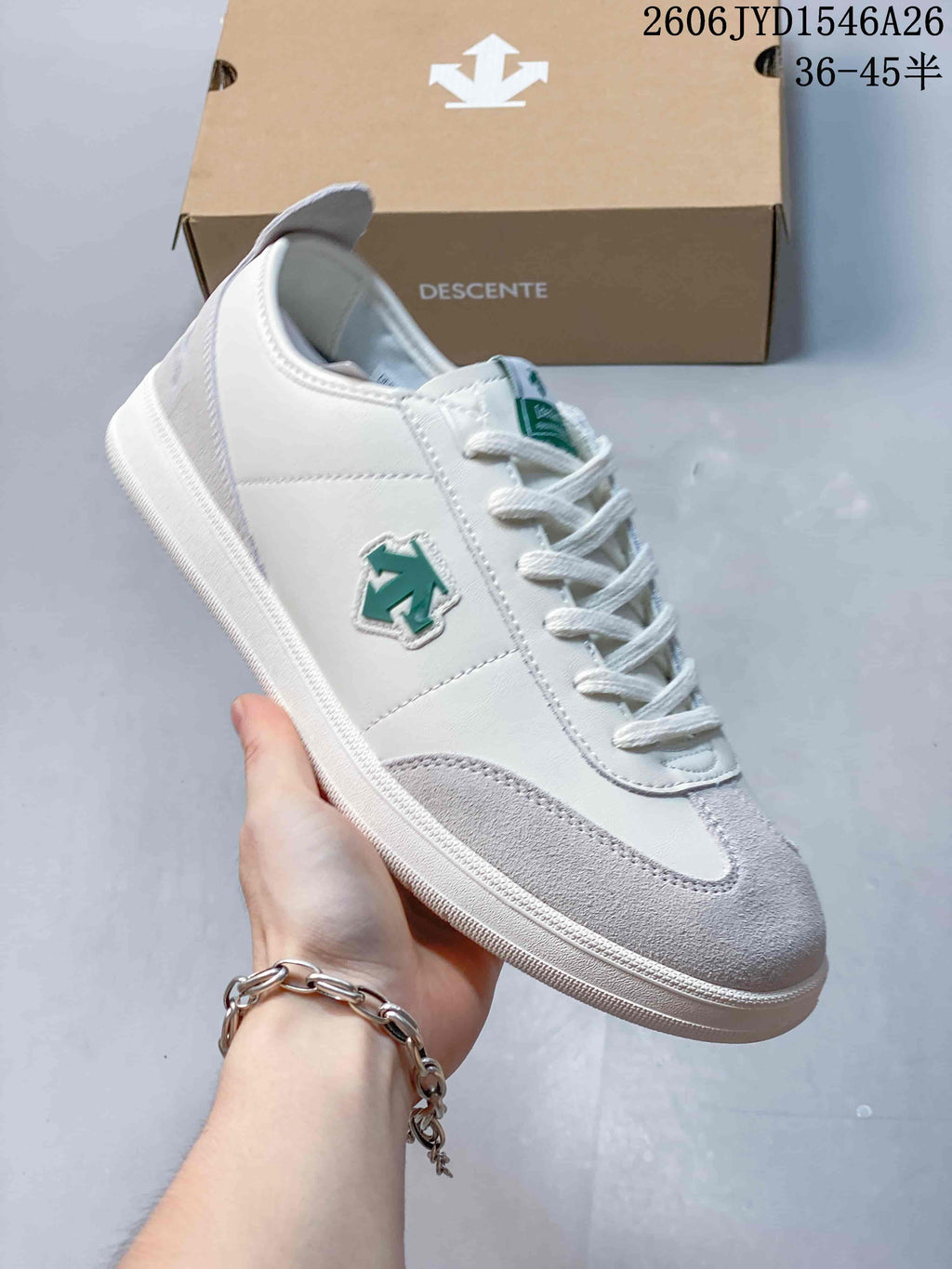 Close-up of a white Descente sneaker with pale gray overlays and a green side emblem.