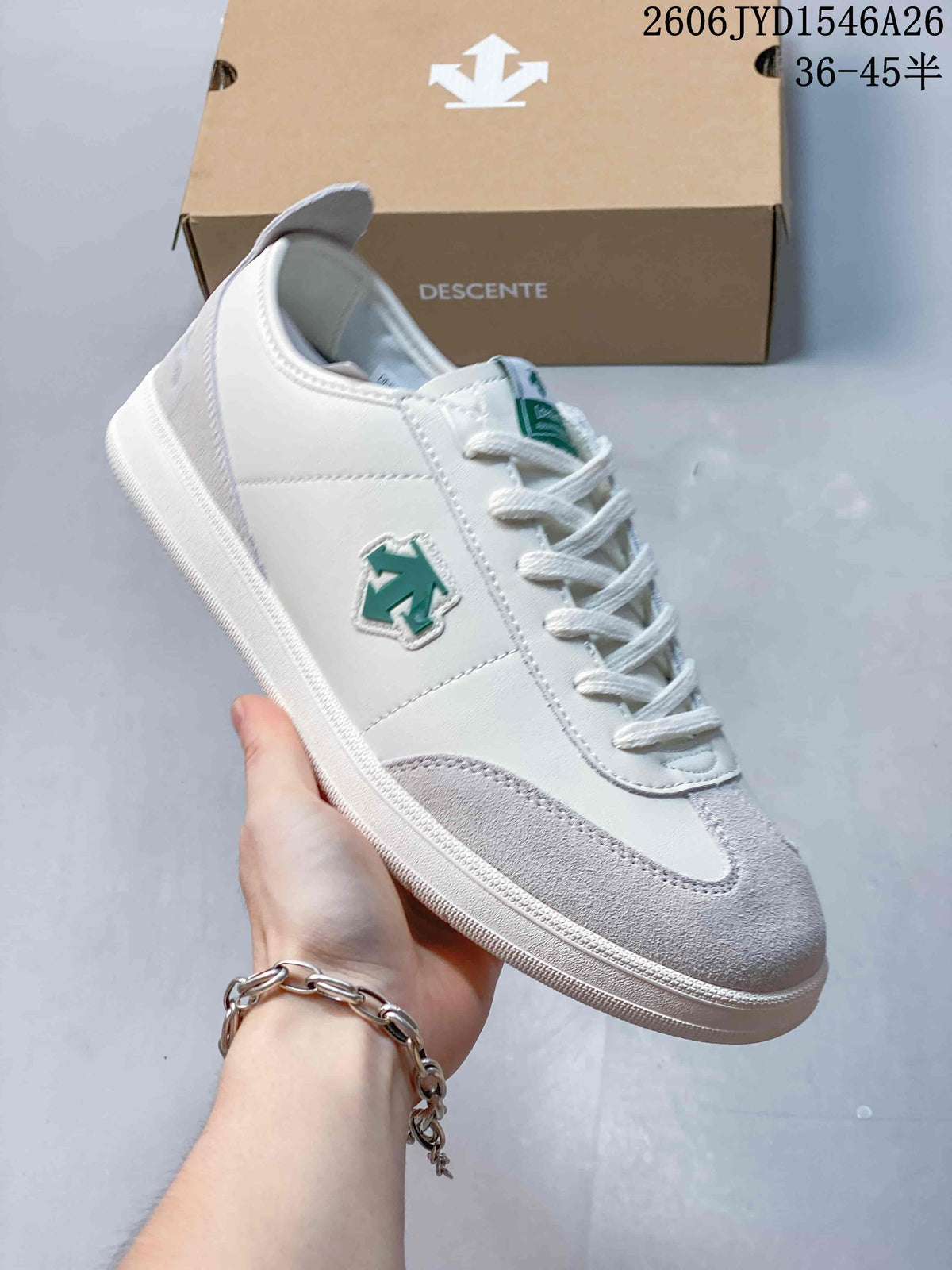 Close-up of a white Descente sneaker with pale gray overlays and a green side emblem.
