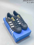 Three Adidas Superstar sneakers in white and dark gray, shown from the side beside a blue shoe box.