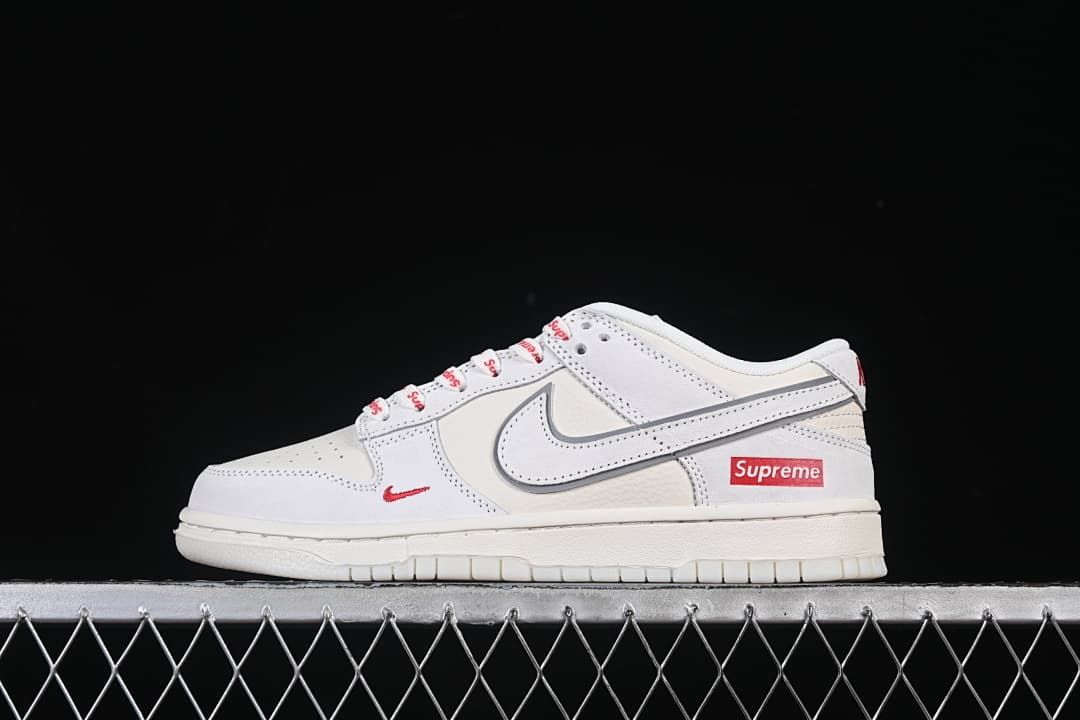 Side view of a white and grey Nike SB Dunk Low with red accents and Supreme-branded heel detail