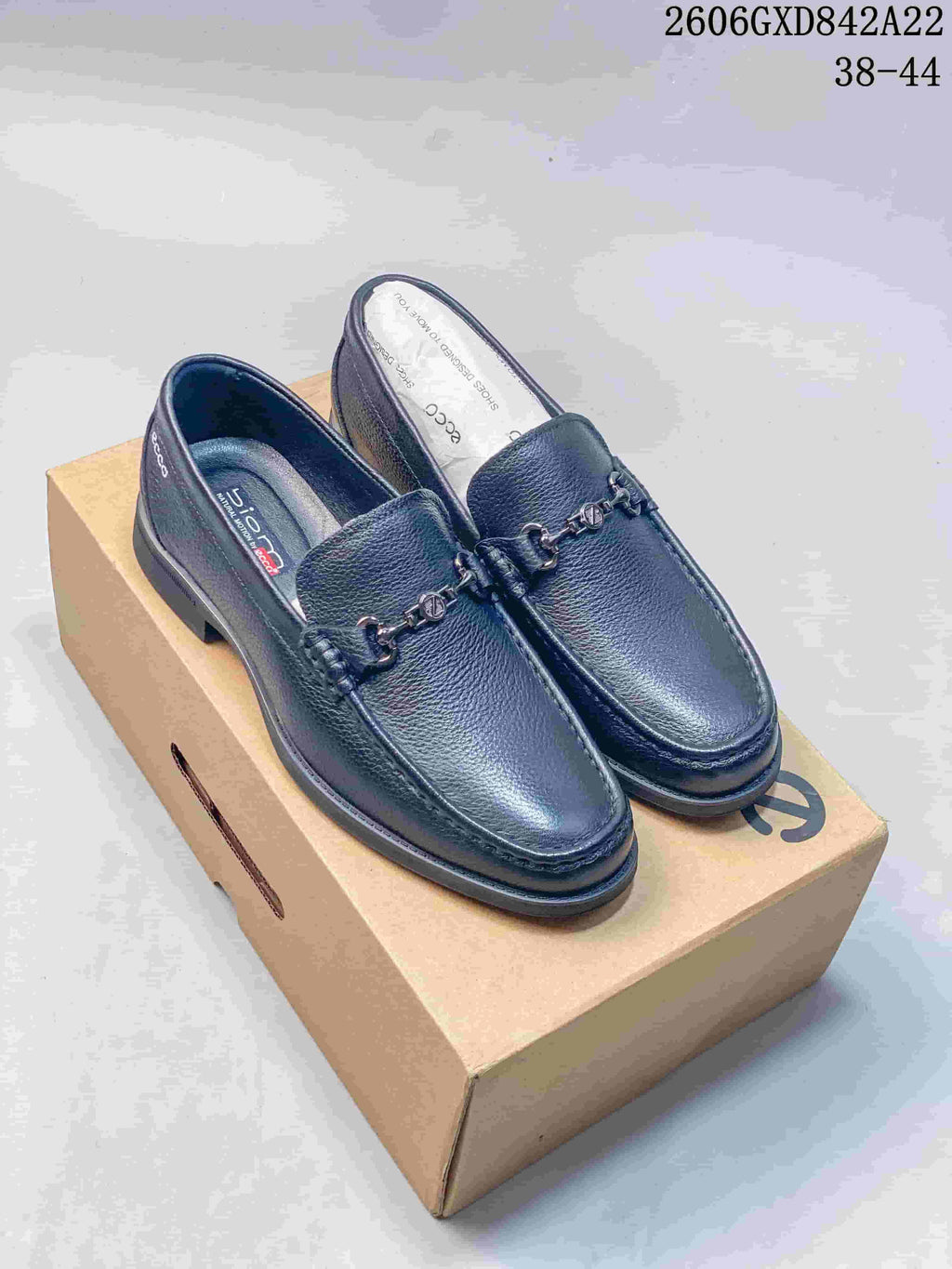 Black slip-on loafers with moc-toe stitching and metal bit detail on a shoe box.