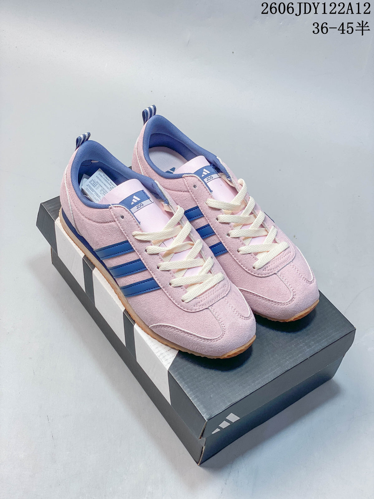 Pair of pink Adidas Originals VS JOG 2.0 sneakers with blue stripes and cream laces, shown on a shoebox