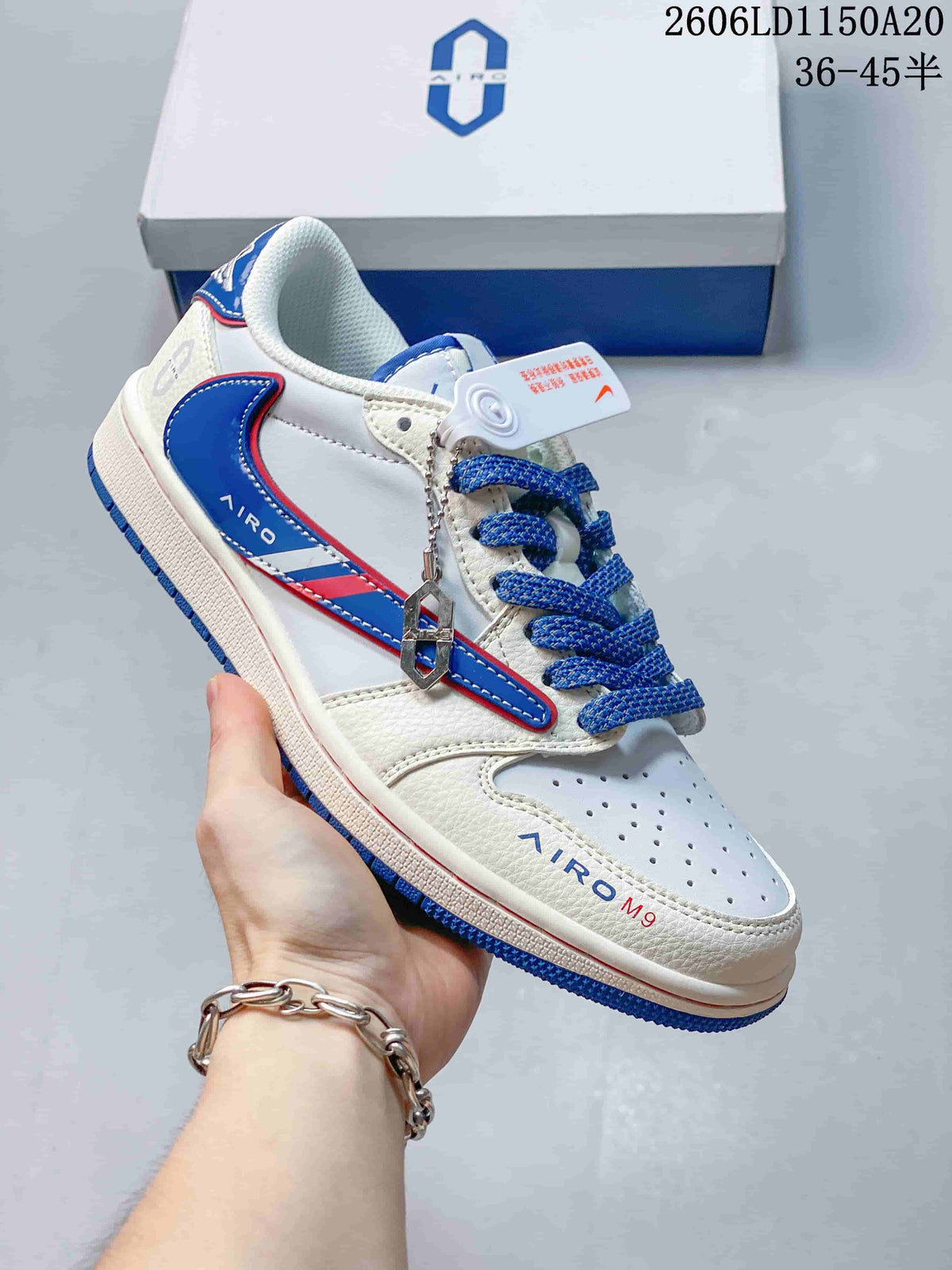 Close view of a white low-top sneaker with blue laces, blue-red side detailing, and a decorative charm.