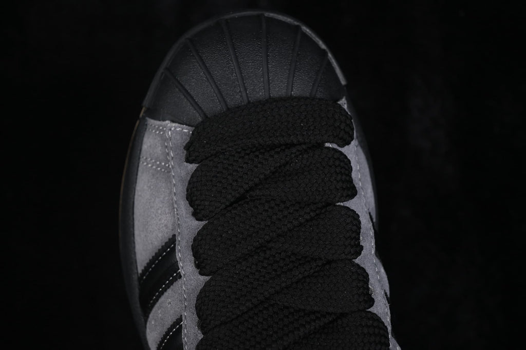 Close-up of the black laces, shell toe, grey upper, and partial side stripe detail.