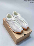 Pair of white and light gray Descente lace-up sneakers with gum-colored soles, shown on a branded box.