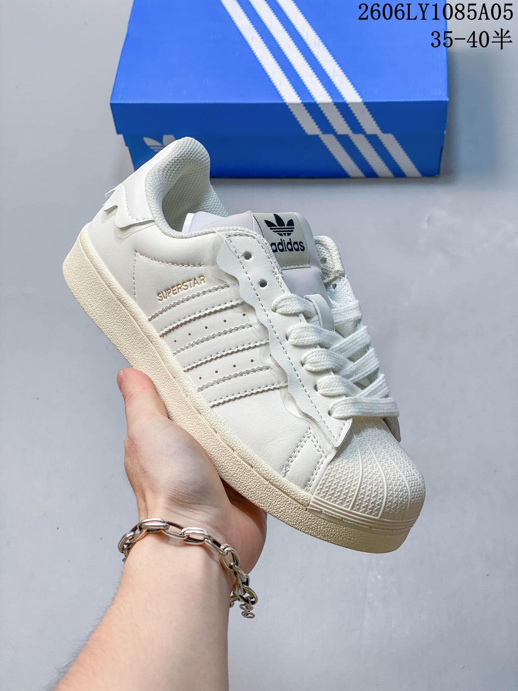 Angled side view of a cream Adidas Superstar sneaker with shell toe and three stripes