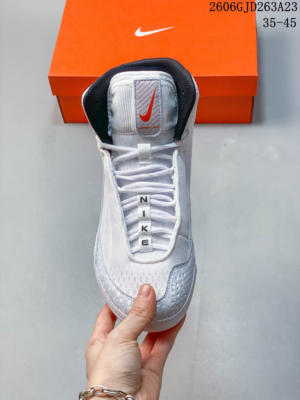Front view of a white and light gray Nike Inflict 4 shoe with black collar lining and orange tongue detail.