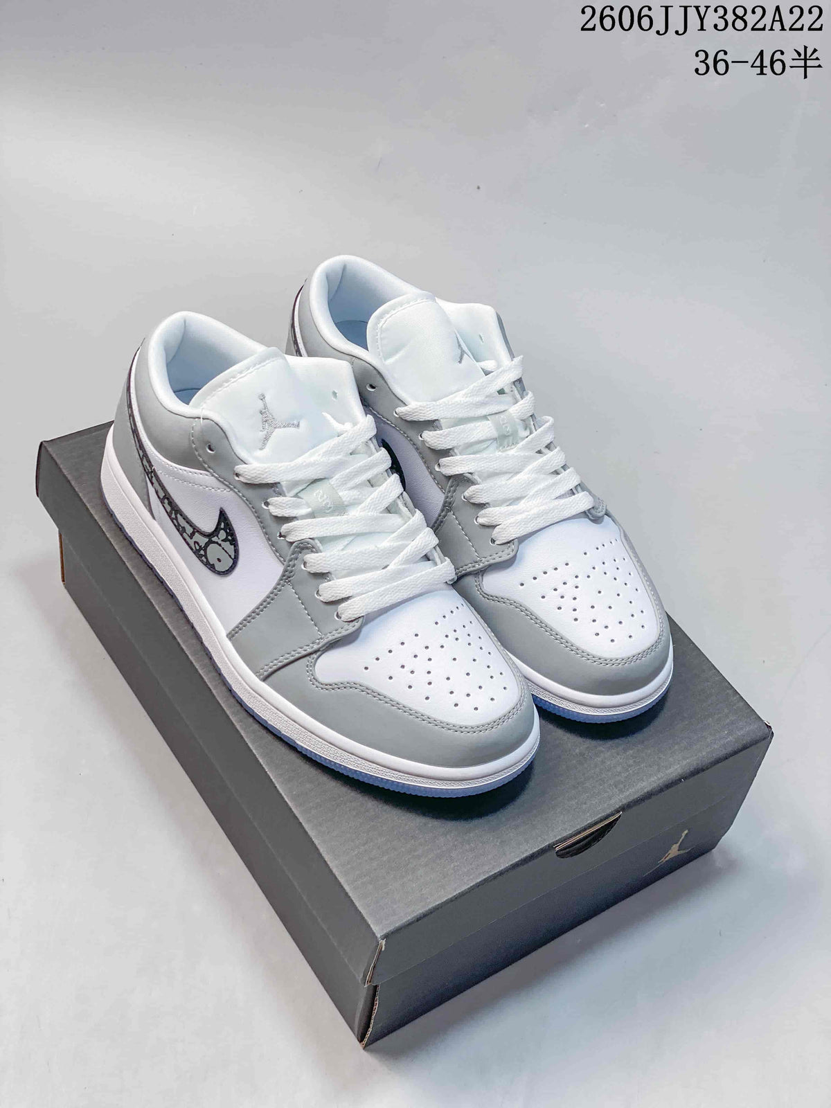 Pair of white and grey low-top Air Jordan 1 sneakers with patterned Swooshes, shown on a box