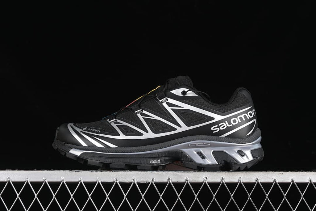 Side view of black and silver Salomon XT-6 GTX sneakers against a dark background.
