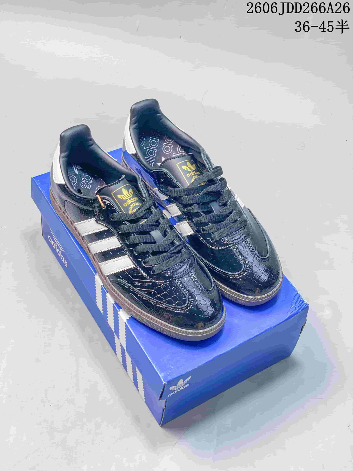 Pair of dark embossed-pattern Adidas Samba sneakers with white side stripes and gum-tone soles, shown on a blue shoe box.