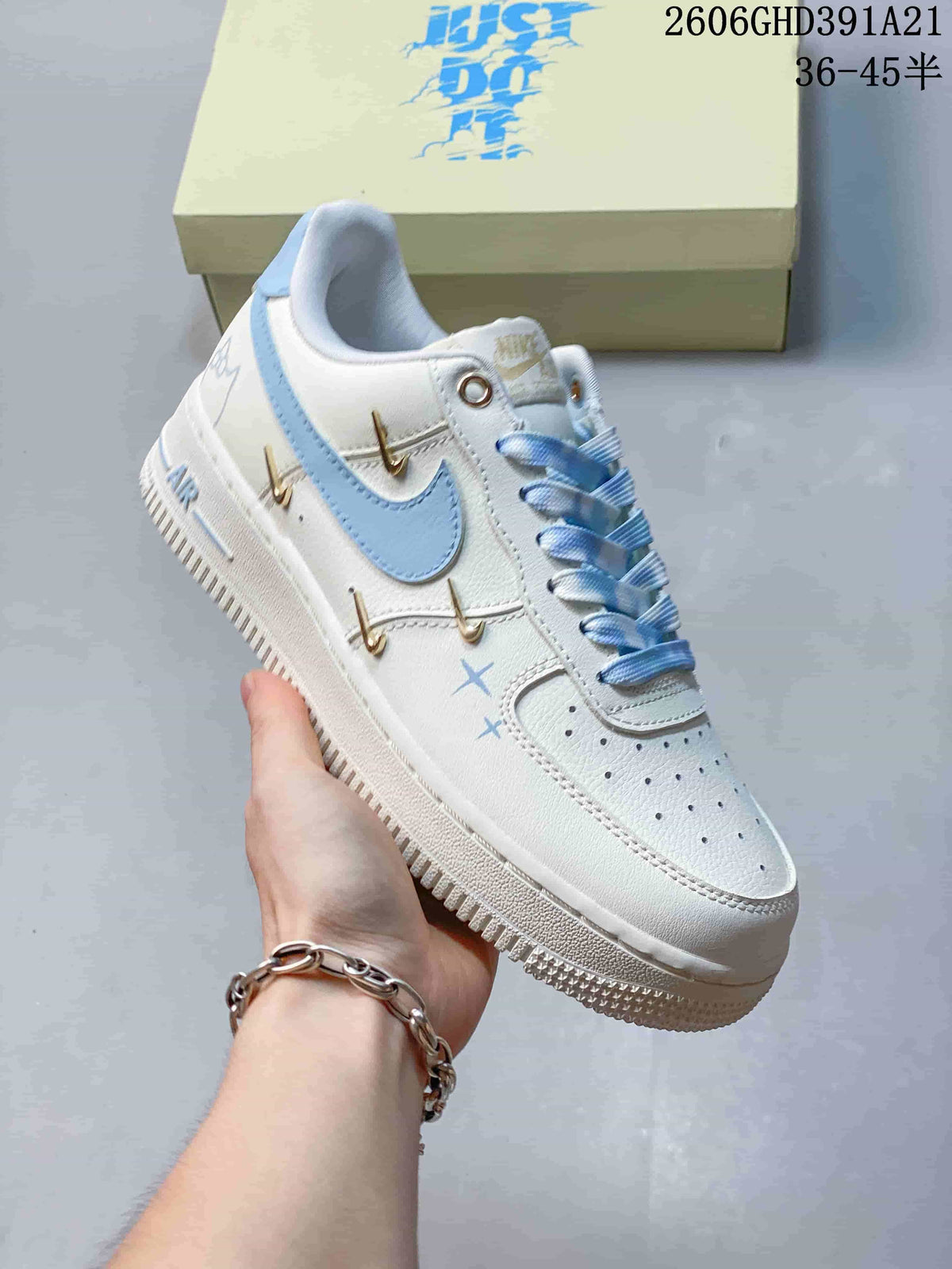 Side view of a white sneaker with a light-blue Swoosh, patterned laces and gold-tone decorative attachments.
