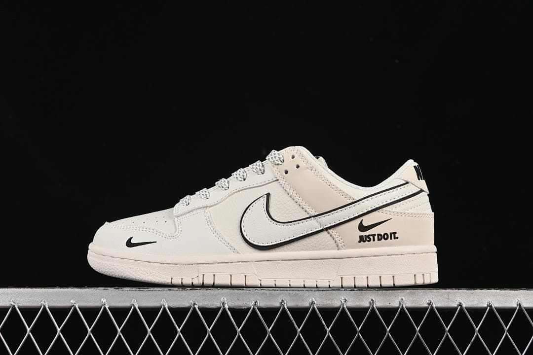 Side view of an off-white Nike SB Dunk Low with black Swoosh details and a heel-side “JUST DO IT.” graphic.