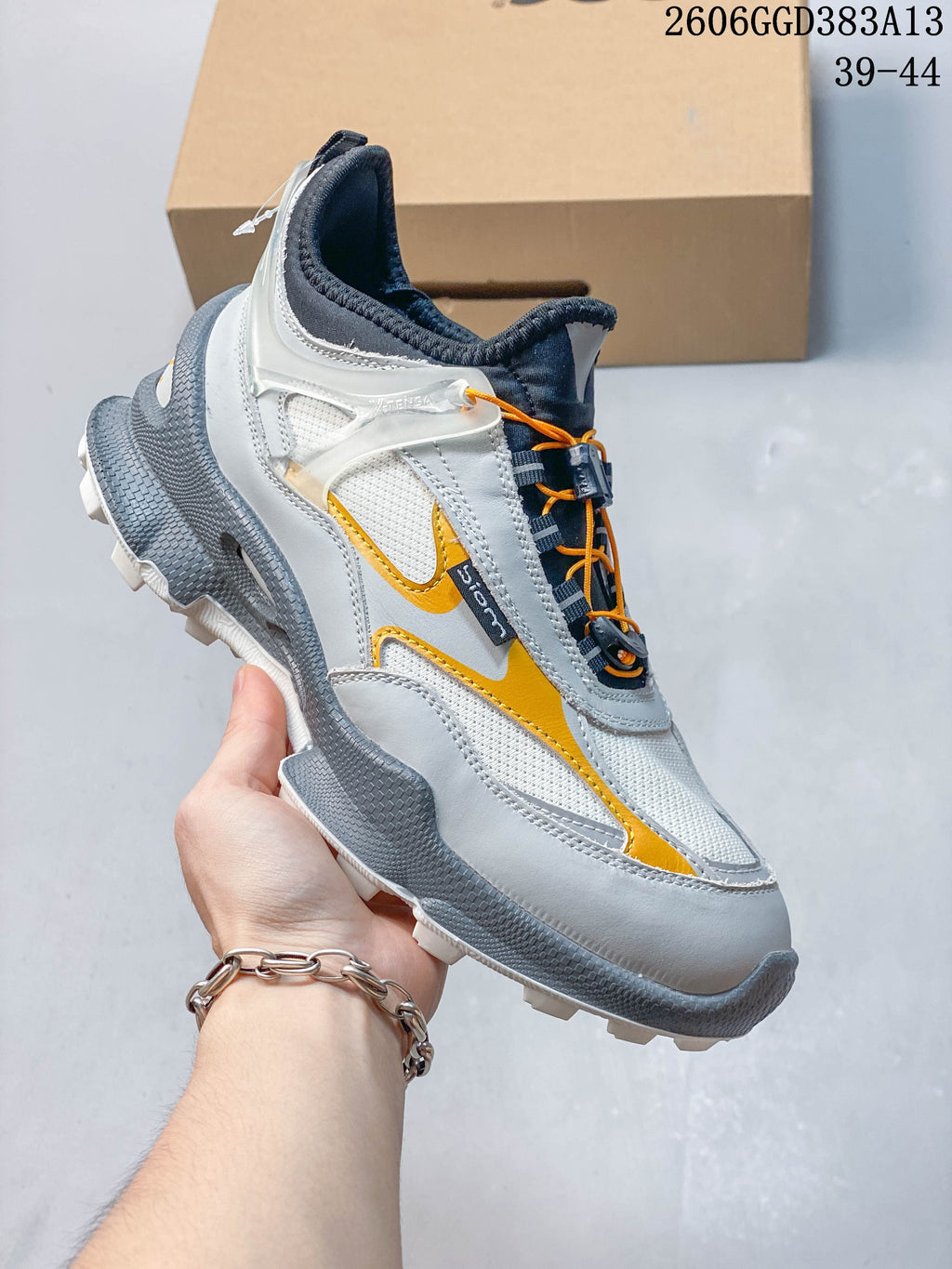 Side profile of the white and gray sneaker with orange accents and a rugged outsole.