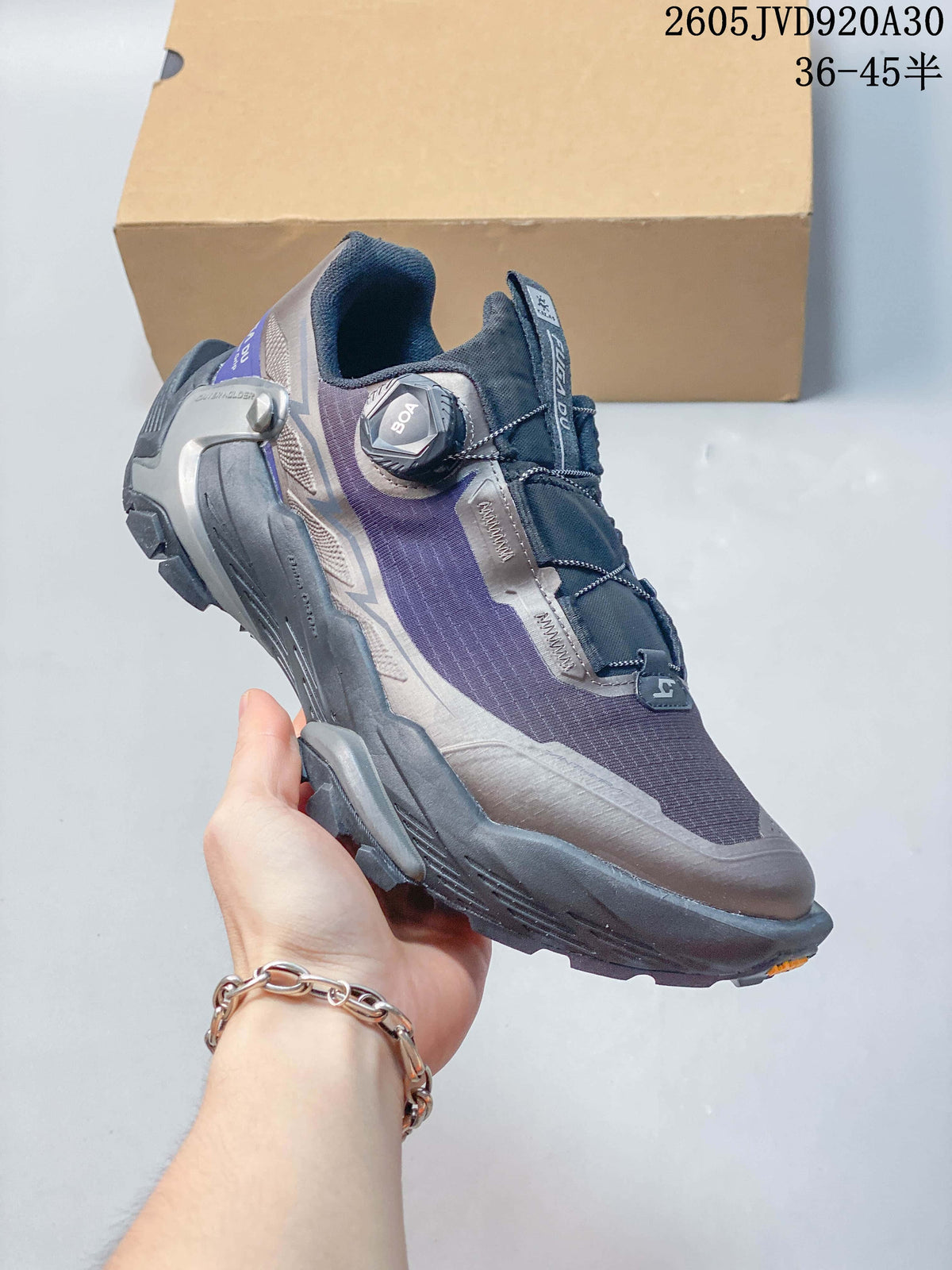 Angled side view of one gray and purple trail shoe with a rotary closure and rugged tread.