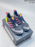 Pair of dark gray Adidas Ultraboost-style shoes with coral-red stripes, neon yellow heel pieces, and white lugged outsoles on a shoebox
