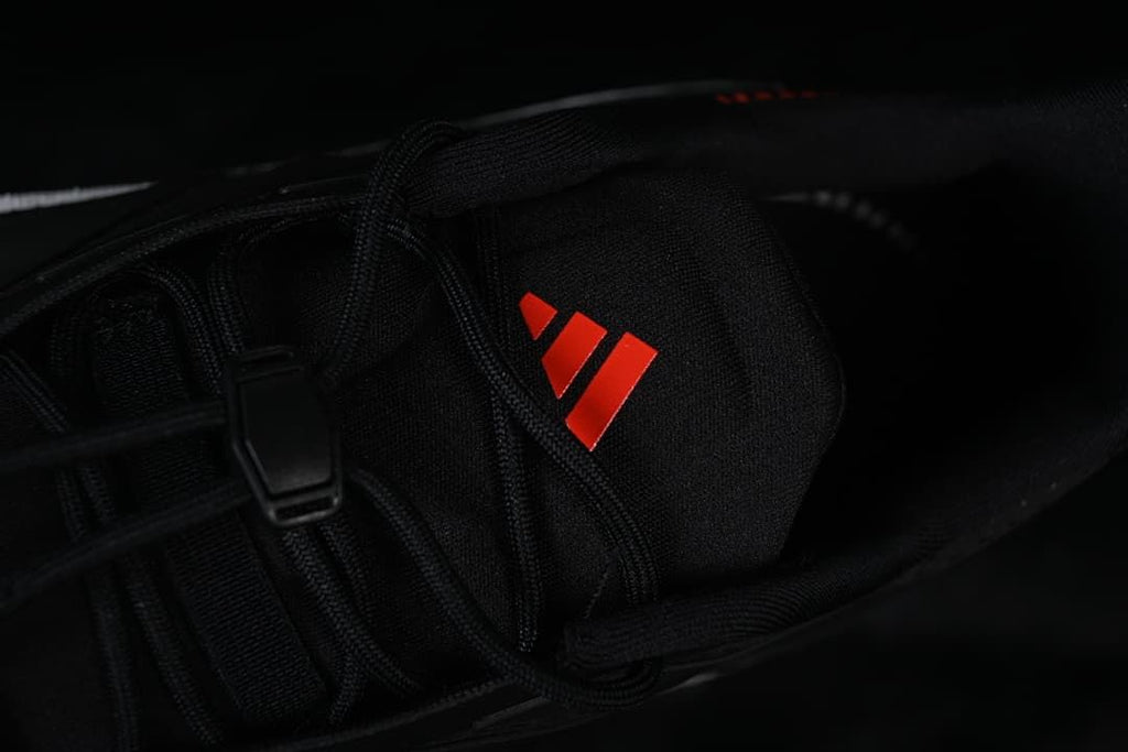 Close-up of the black tongue with a red adidas logo and lace detail.